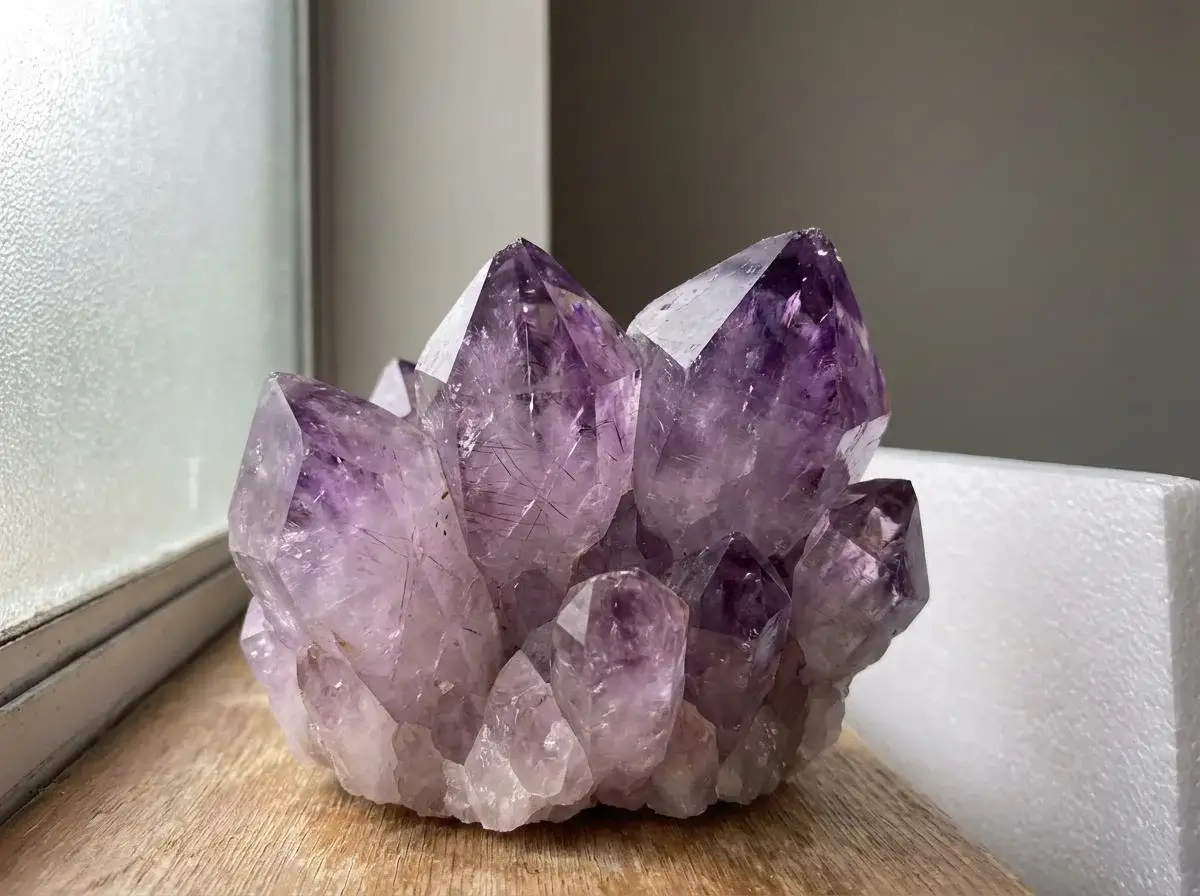 Bližnji posnetek naravnega ametista ob oknu, na katerem so vidni nežni barvni prehodi in kristalna struktura.