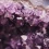 Amethyst crystal cluster on a decorative surface under soft lighting.