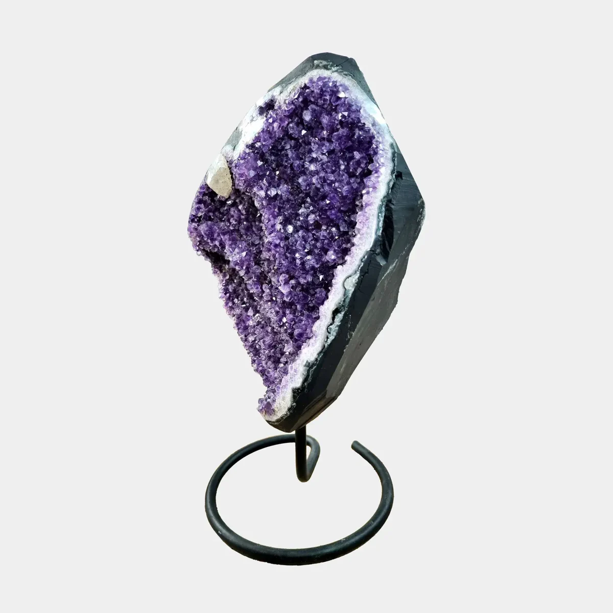 Pogled s strani na razkošno ametistno geodo na kovinskem stojalu, ki razkriva globino kristalov in naravne obrise kamnine.