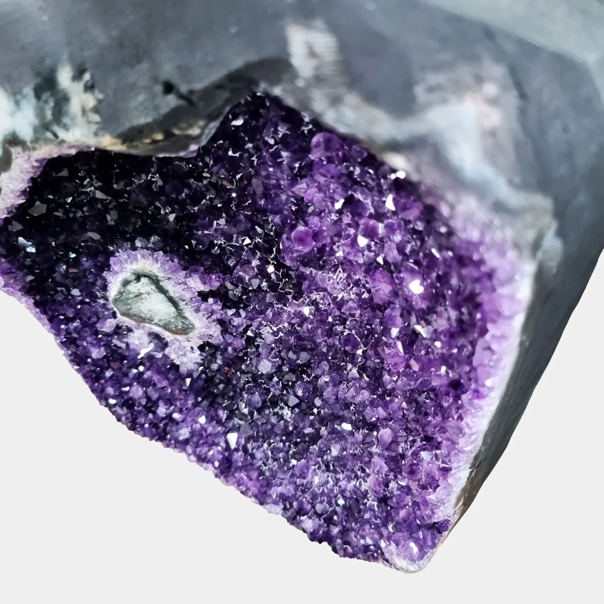 Povečan pogled prikazuje živahne vijolične kristale z naravno formacijo v središču in izjemno strukturo kristalnih ploskev.