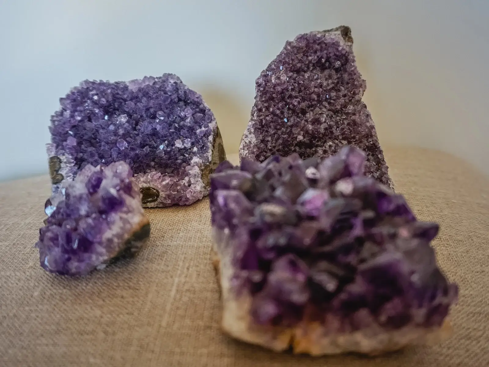 Skupina naravnih ametistnih grozdov različnih velikosti, razstavljenih na nevtralni površini in prikazujących globoko vijolične kristale ter surovo mineralno strukturo.