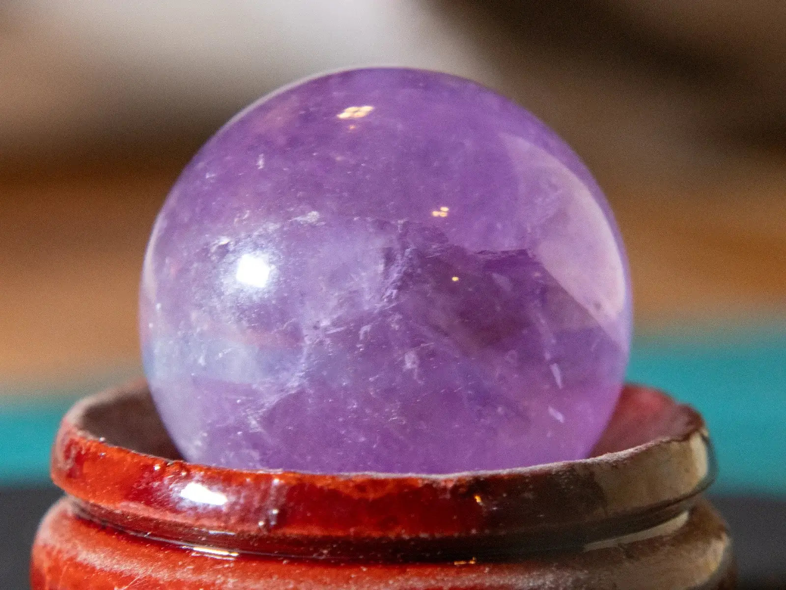 Makro pogled na spolirano ametistno kroglo z bogatimi vijoličnimi odtenki, ki počiva na lesenem podstavku.