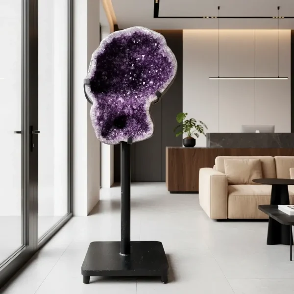 Velika ametistova geoda na črnem stojalu, razstavljena v modernem luksuznem preddverju z umirjenimi toni in elegantnim pohištvom.