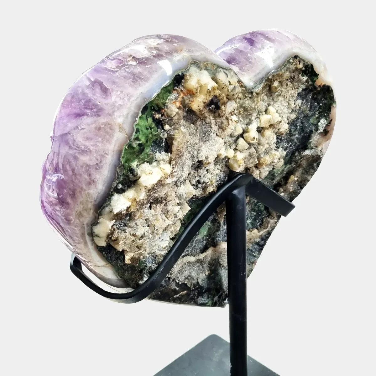 Zadnji pogled, ki prikazuje surovo mineralno površino in zeleno matrico srčasto oblikovanega ametistovega grozda.