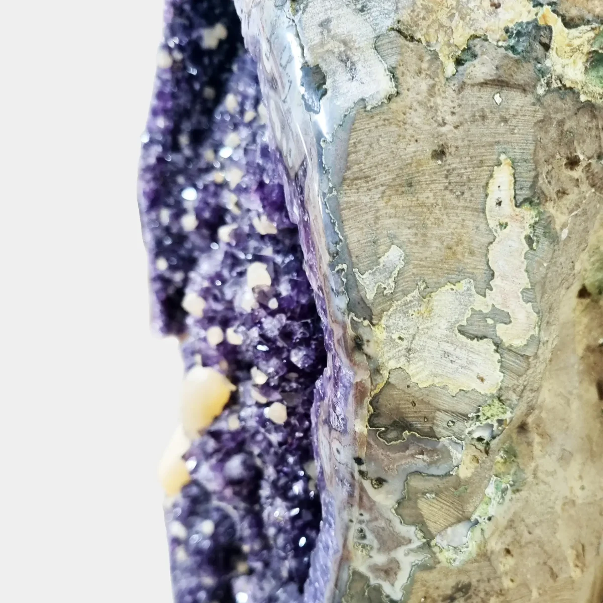 Podroben pogled na spolirano zunanjo plast in mineralno matrico, ki obdaja votlino z ametistovimi kristali.