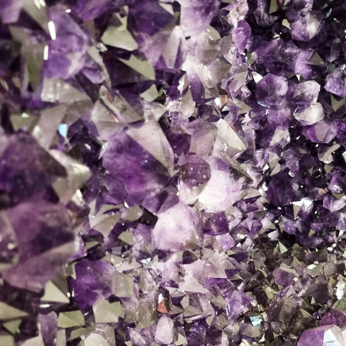 Podroben bližnji pogled na globoko vijolične ametistove kristale z ostrimi fasetami in naravnim, iskrivim sijajem.