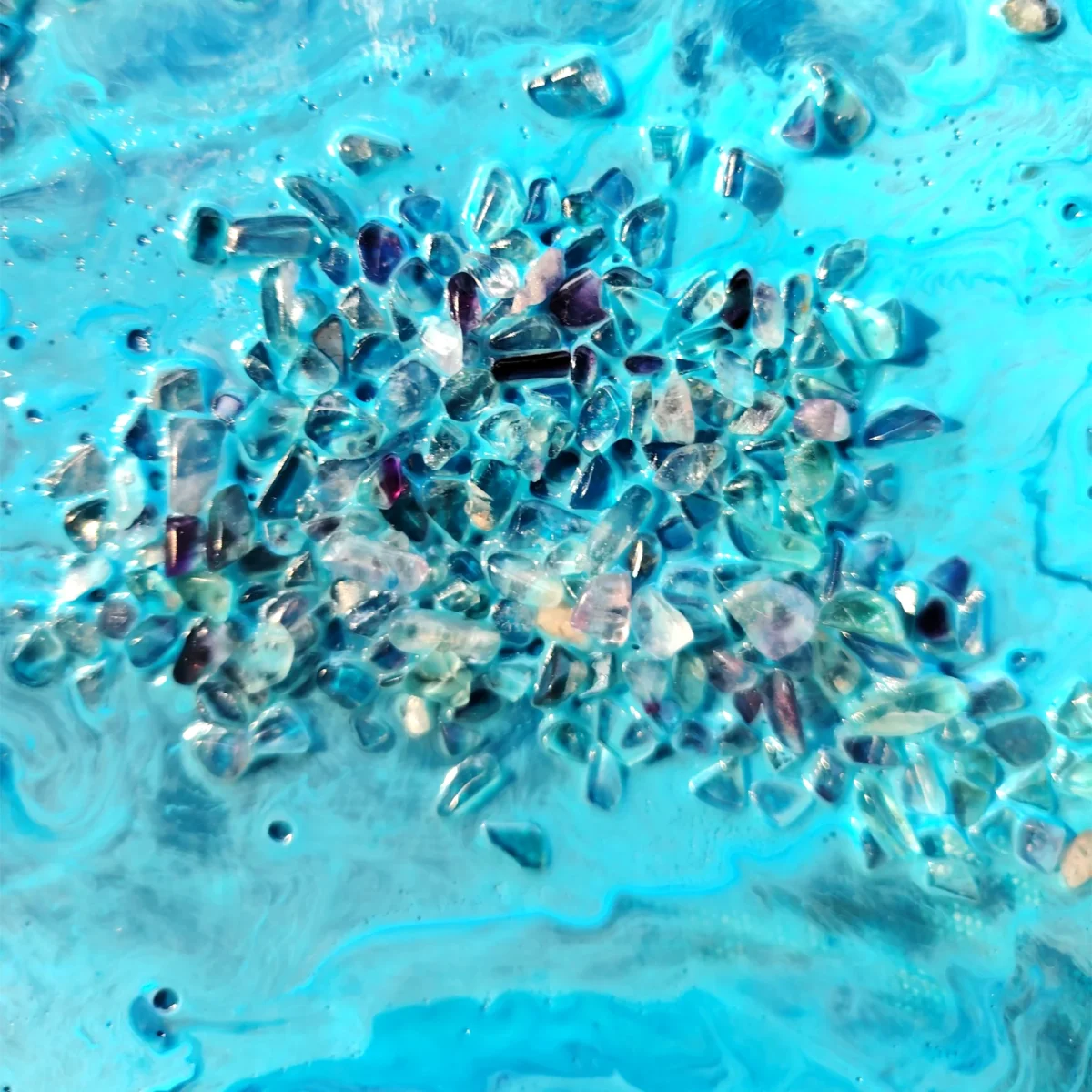 Close-up of pale blue crystal fragments against layered turquoise and blue paint