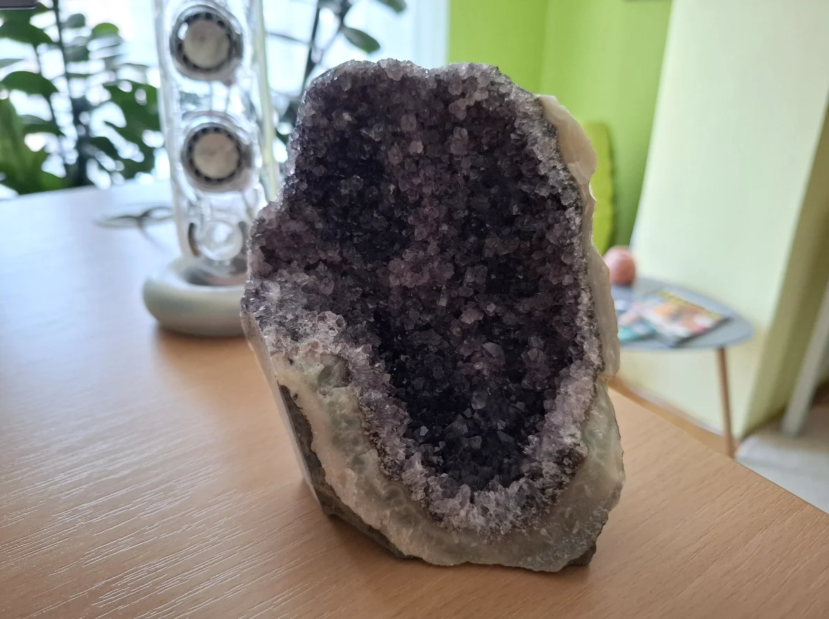 Small natural amethyst geode with deep purple crystals displayed on a wooden desk in a home office