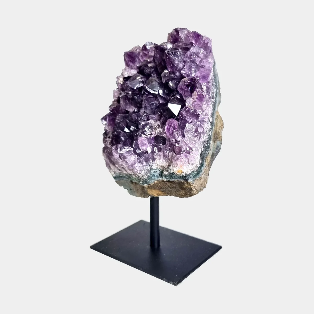 Angled front view of an amethyst cluster on stand with purple crystals and a natural stone base.