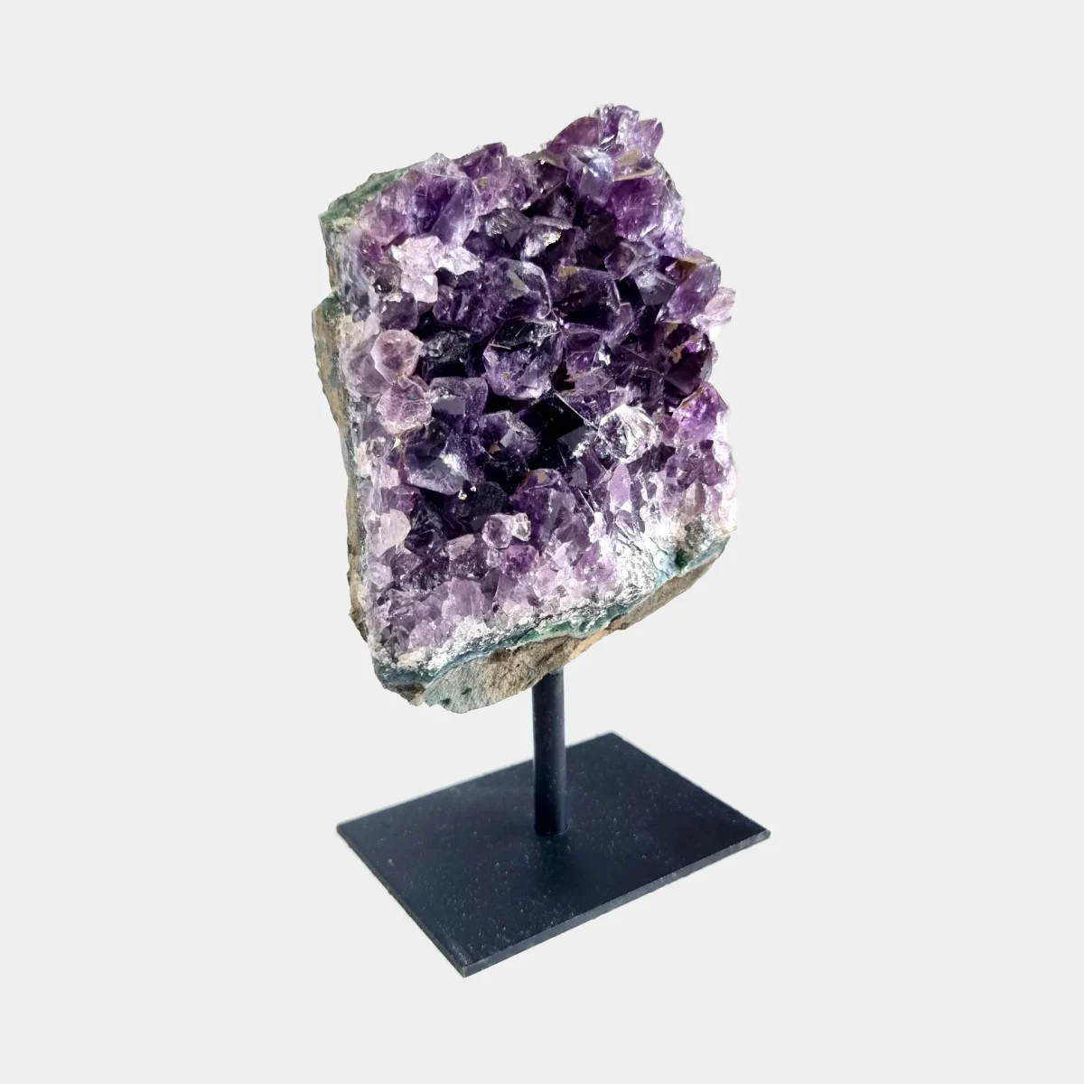 Side angle view of an amethyst cluster on a black metal stand showing violet crystals and natural stone.