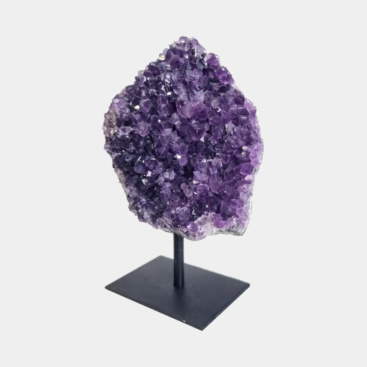 Angled front view of an amethyst cluster on stand with purple crystals and a black metal base.