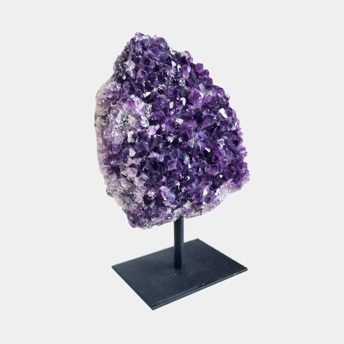 Side angle view of an amethyst cluster on a black metal stand showing violet crystal points and natural stone.