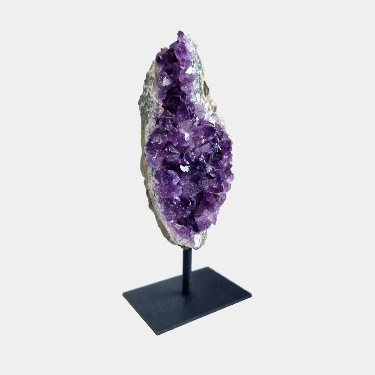 Side view of an amethyst cluster on a black metal stand showing violet crystals and the natural stone profile.