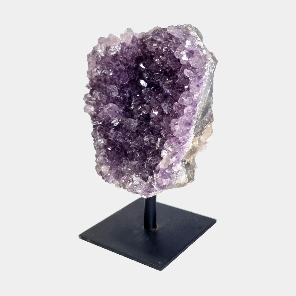 Angled front view of an amethyst cluster on stand with purple crystals and a pale natural stone side.