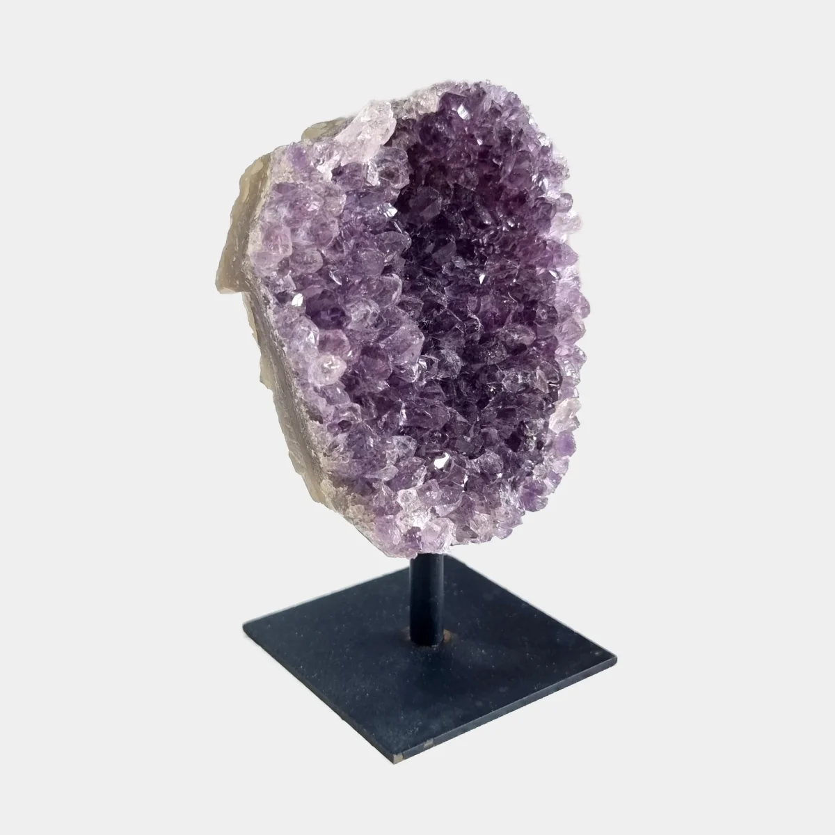 Side angle view of an amethyst cluster on a black metal stand showing purple crystals and natural stone.