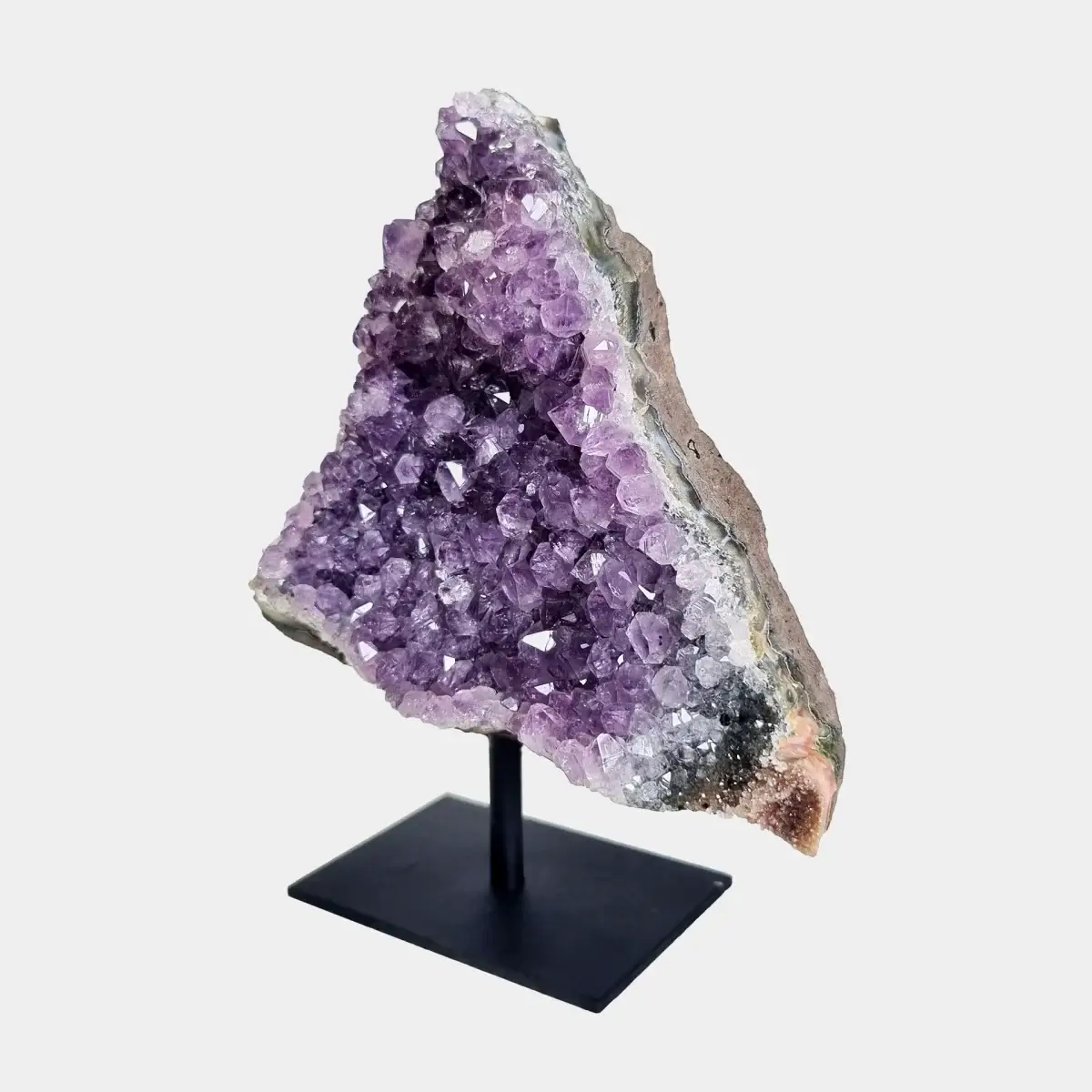 Angled front view of an amethyst cluster on stand with purple crystals and a natural stone side.