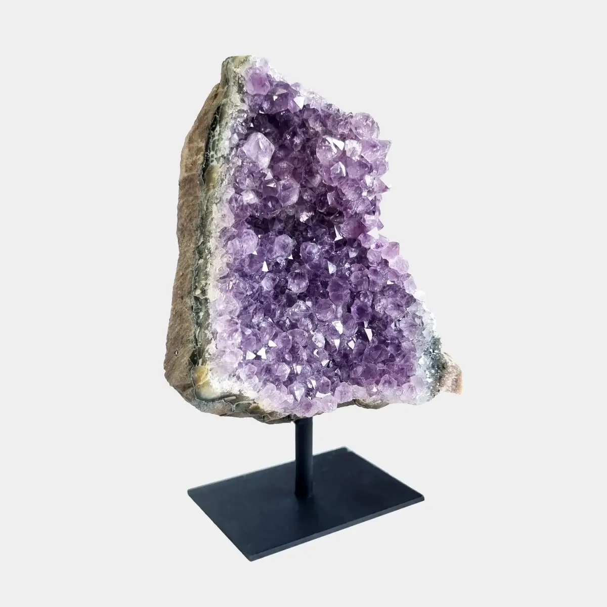 Side angle view of an amethyst cluster on a black metal stand showing violet crystals and natural stone.