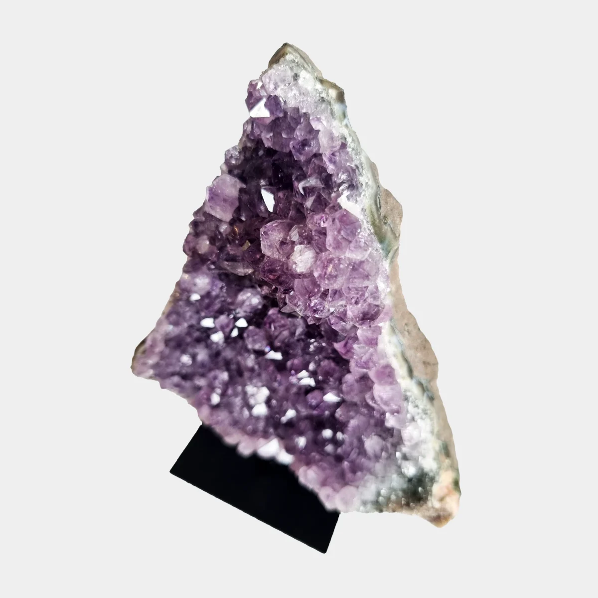 Angled detail view of an amethyst cluster on stand showing violet crystals, pale quartz, and natural stone edges.