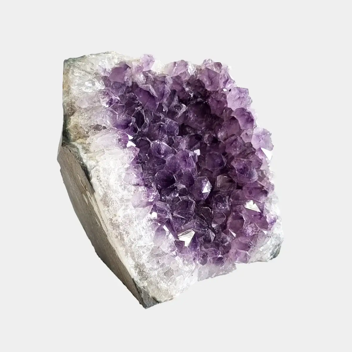 Side view of a small amethyst geode showing purple crystals, white quartz, and the natural stone base.