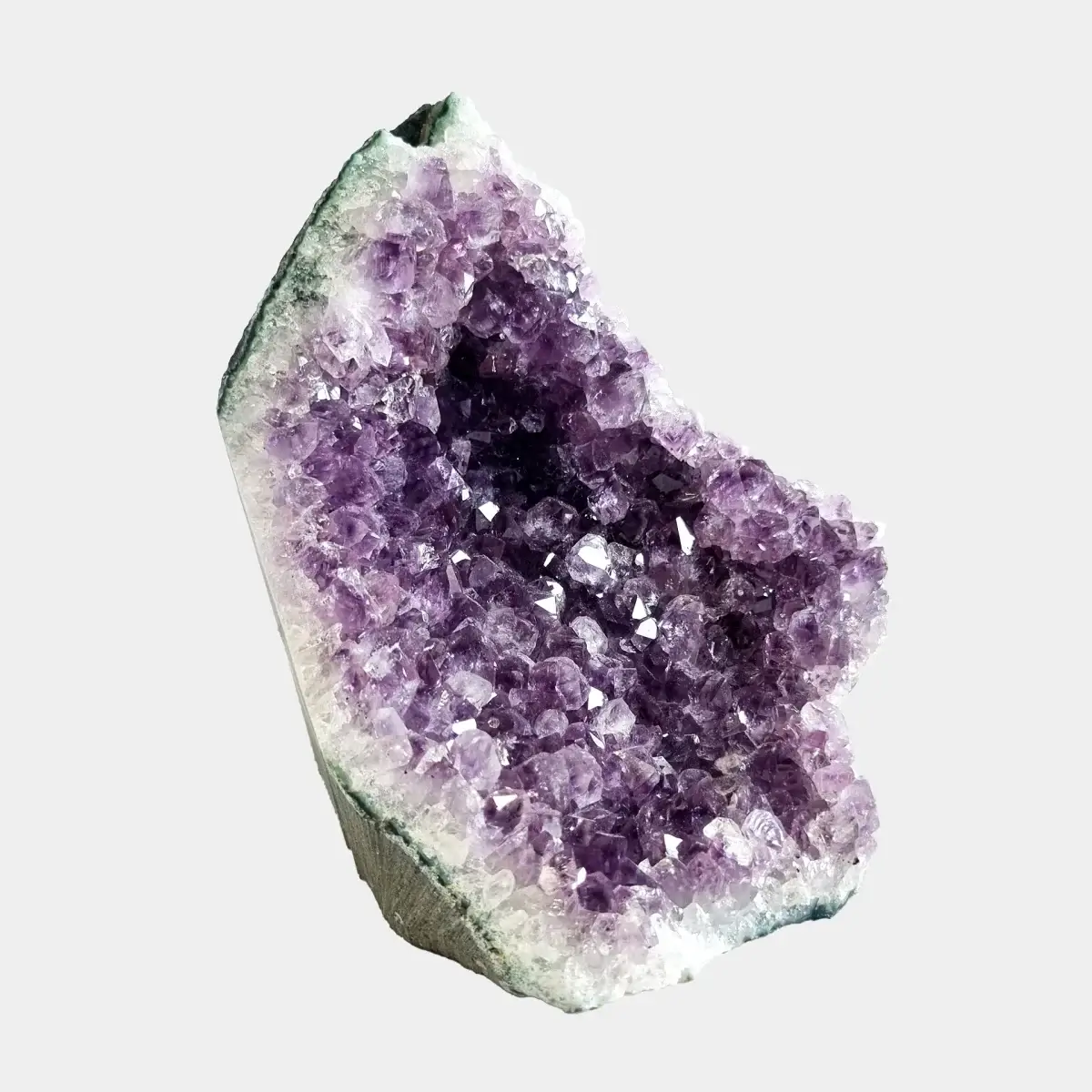 Side view of a small amethyst geode showing violet crystal points, white quartz, and the cut stone exterior.