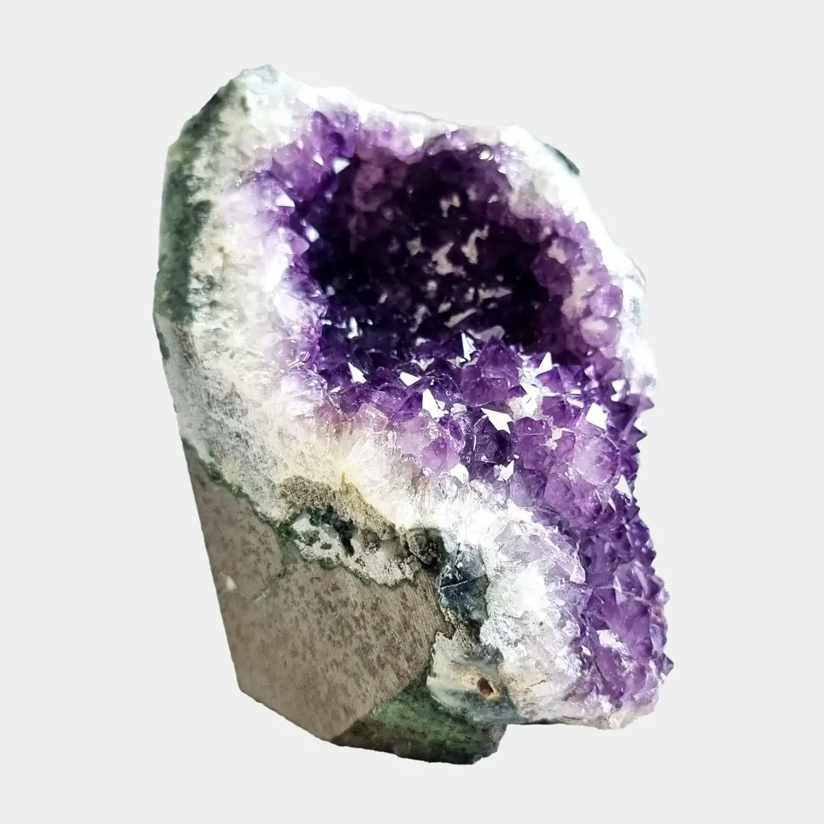 Side angle view of a small amethyst geode showing violet crystals, white quartz, and the natural stone exterior.